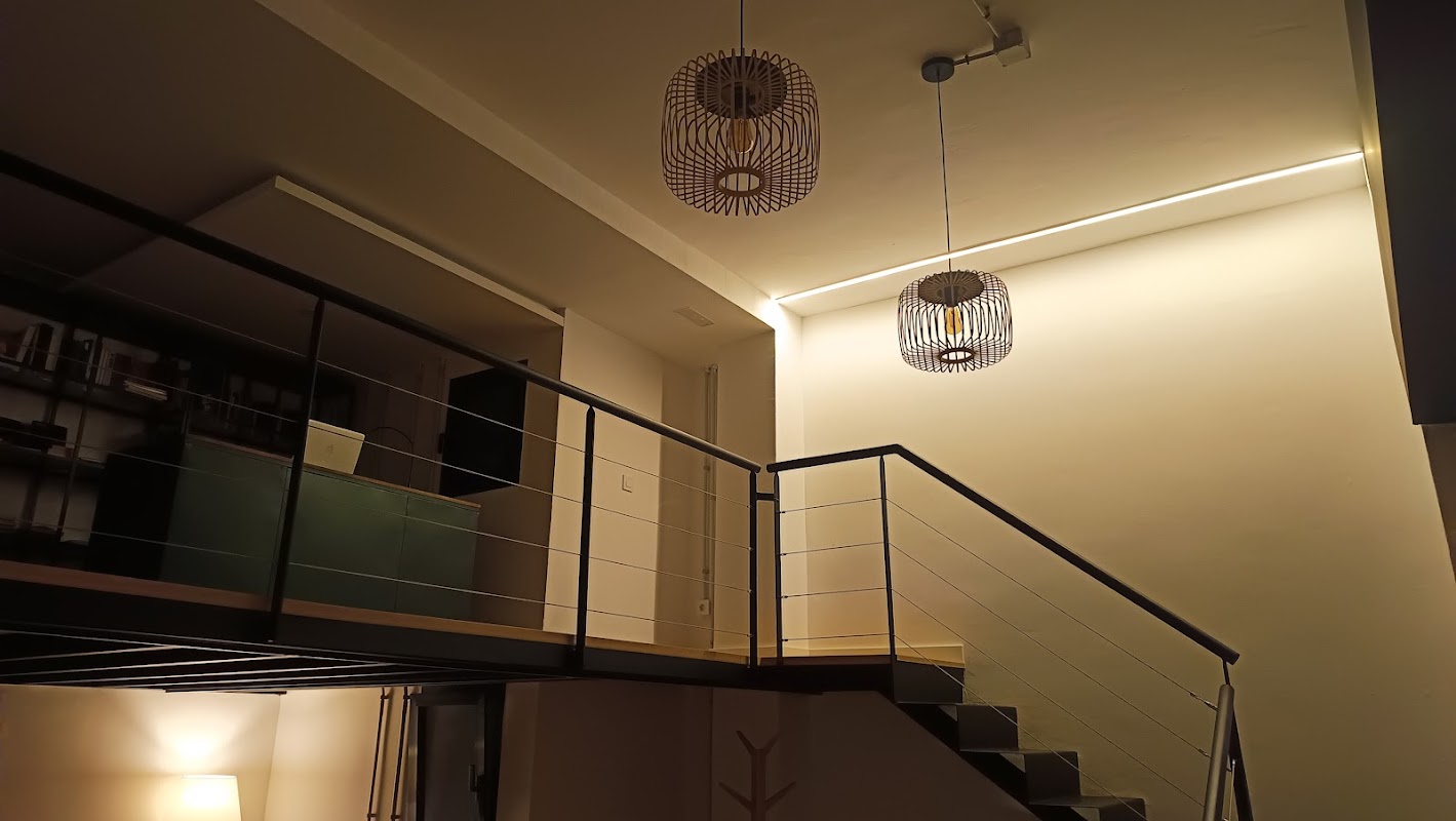 Loft moderno con escaleras, barandilla metálica, lámparas colgantes geométricas e iluminación LED cálida